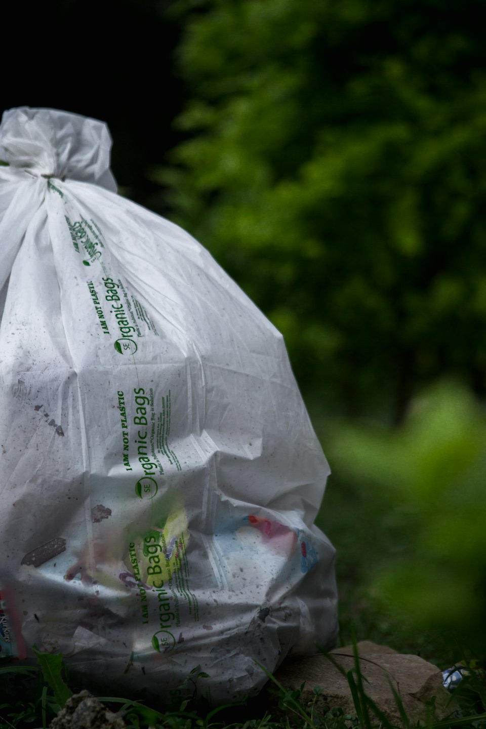 Organic waste bag filled with refuse sitting on the earth.
