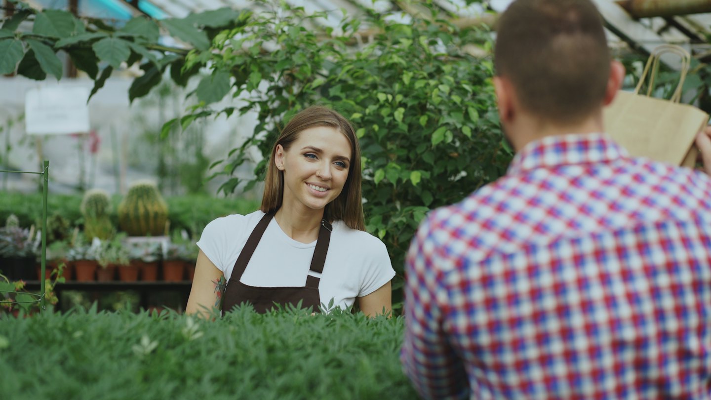 Greenhouse worker smiles at a customer making a purchase.